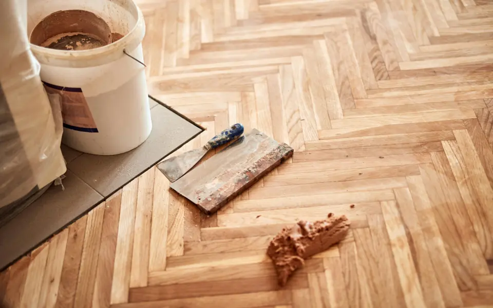Parquet en chevrons en cours de pose, avec les outils et un seau de colle posés sur les lames