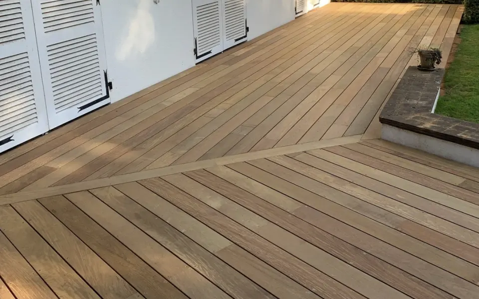 Terrasse en bois le long d’une façade blanche à volets, avec des lames posées en deux sens