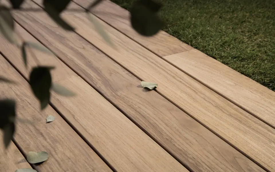 Lames de terrasse en bois clair près d’une pelouse, avec des feuilles posées dessus
